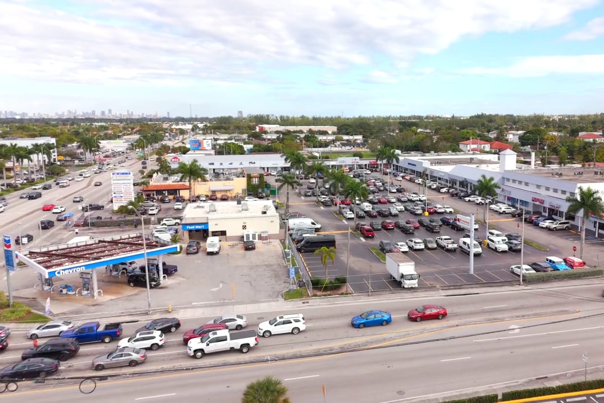 Aerial of a fuel station beside a strip center on a busy commercial corridor