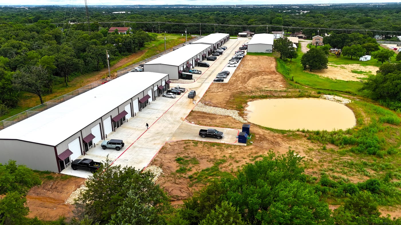 White flex buildings beside raw land and a detention pond