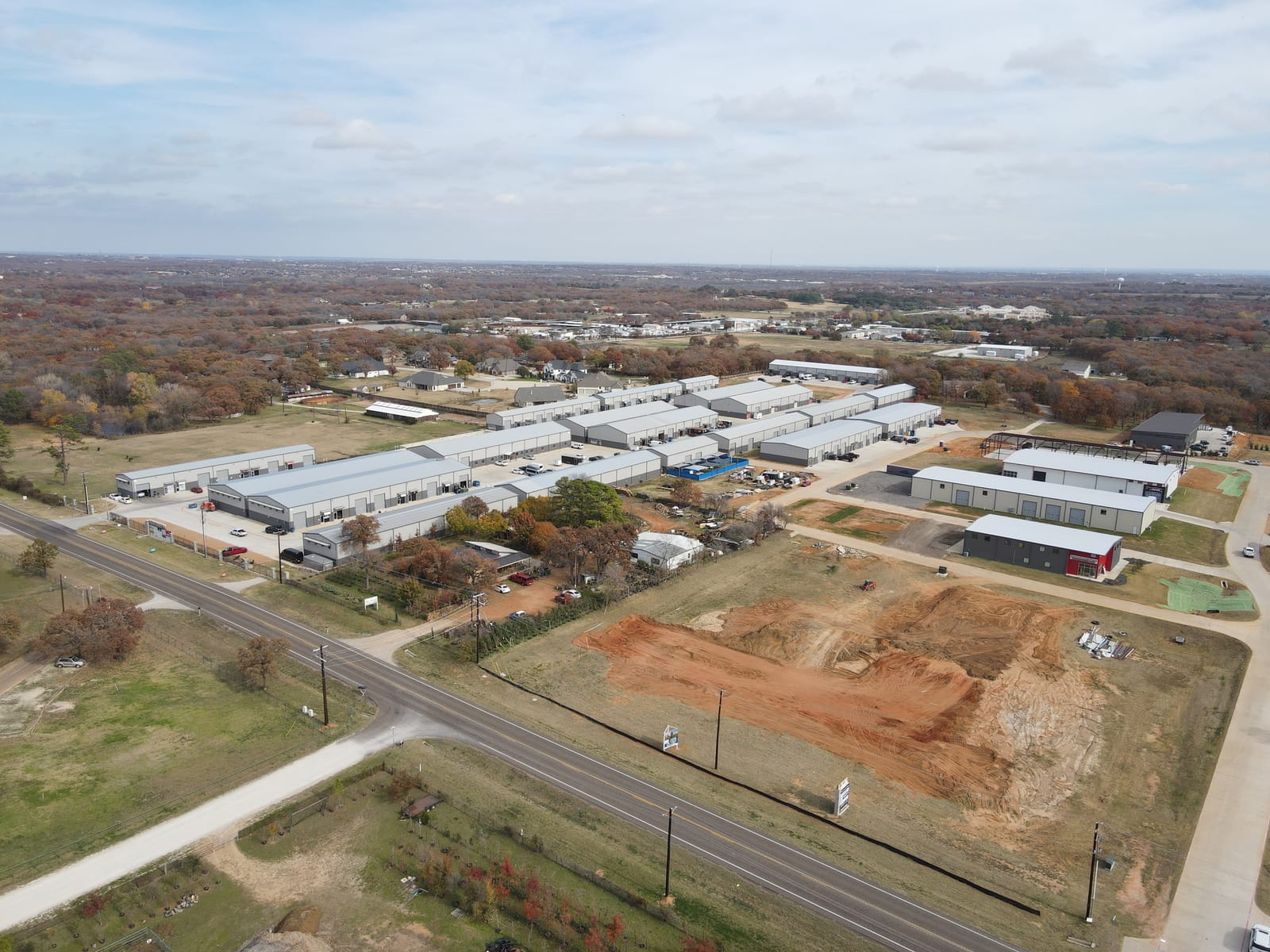 Aerial view of a graded site beside a 2-lane highway, with a flex park and neighborhoods behind it